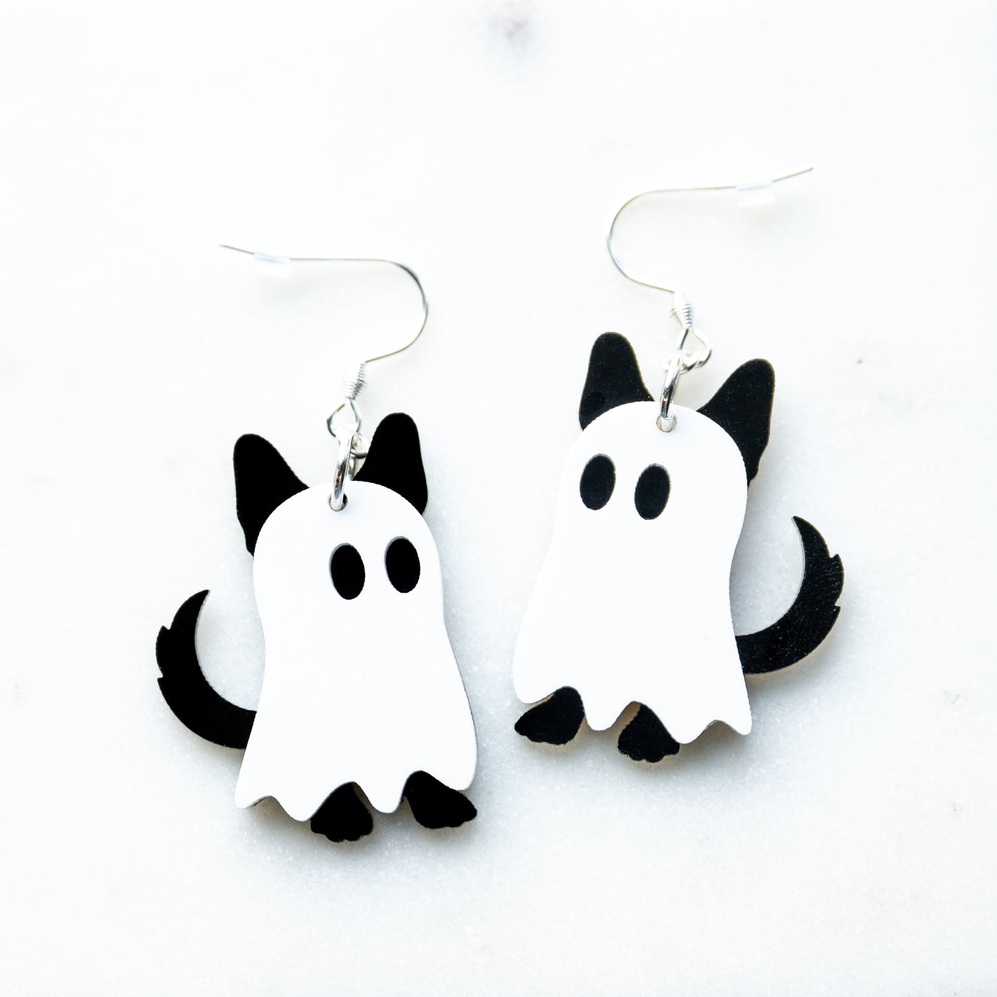 A pair of white and black ghost-shaped dangle earrings with dog ears, feet and tail, designed to look like ghosts dogs with fish hook hardware on a white background.