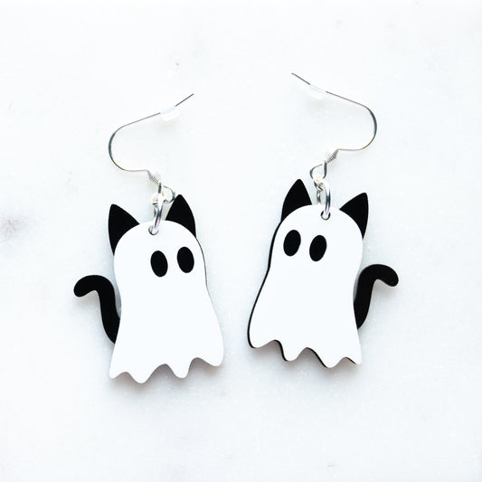 A pair of white and black ghost-shaped dangle earrings with cat ears and tail, designed to look like cat ghosts with fish hook hardware on a white background.