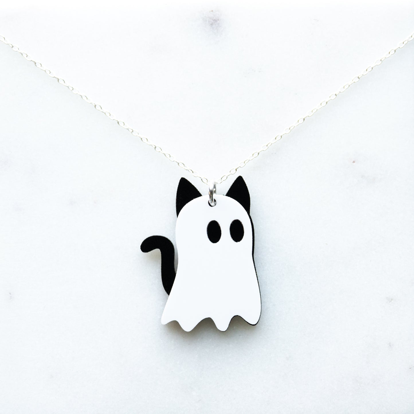 A white and black ghost-shaped acrylic necklace with cat ears and tail, designed to look like cat ghosts with a cable chain displayed on a white background.