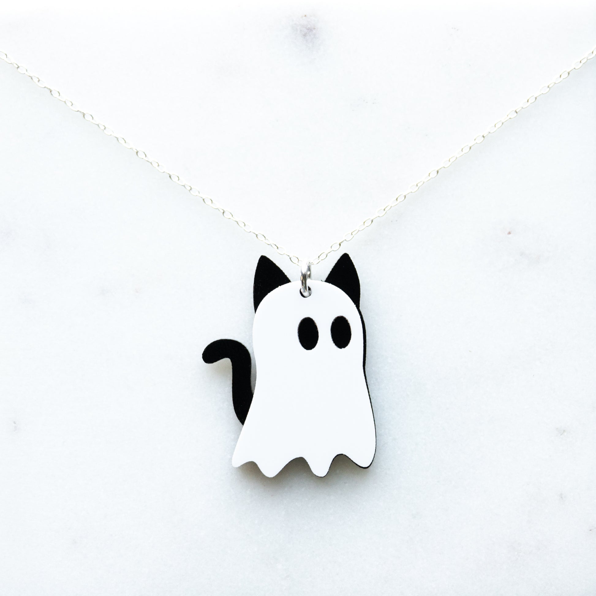 A white and black ghost-shaped acrylic necklace with cat ears and tail, designed to look like cat ghosts with a cable chain displayed on a white background.